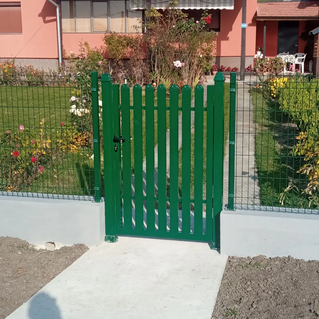 Zelena pešačka kapija sa vertikalnim letvama i zaobljenim vrhovima, uz panelnu ogradu